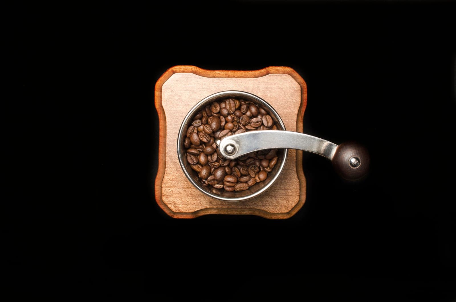 Freshly roasted coffee beans beside a burr grinder on a kitchen counter