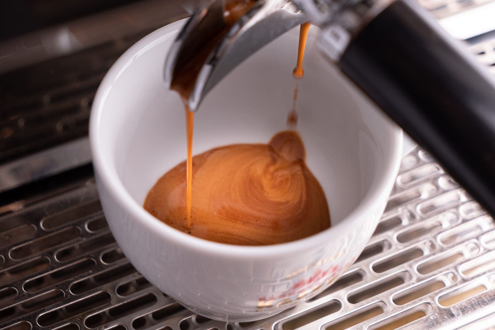 An espresso shot pulling into a cup with fresh crema forming on top